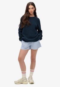 Granatowy sweter dzianinowy, jasnoniebieskie spodenki w paski, kremowe sneakersy i kremowe skarpetki w czerwono-niebieskie paski. Swobodny strój o luźnym kroju.