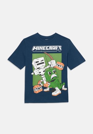 Camiseta de Minecraft azul marino con un esqueleto de dibujos animados sosteniendo un arco y flecha, y un creeper verde sosteniendo bloques de TNT, todo sobre un fondo verde.