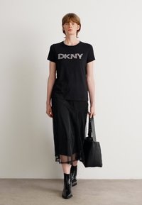 Črna majica DKNY z rožnatim logotipom, v kombinaciji s črno prozorno večplastno krilo in črnimi gležnjarji, ter črno torbo.