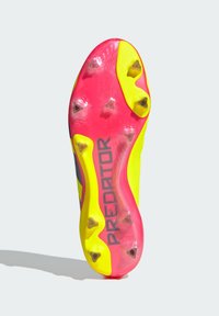 Scarpe da calcio con una suola vivace gialla e rosa, caratterizzate da tacchetti triangolari per la presa, e un logo nero "PREDATOR" lungo il lato.