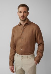 Braunes Langarmhemd aus strukturiertem Stoff mit Knopfleiste. Kombiniert mit hellen Hosen mit flachem Bund und Taschen.
