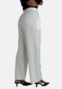Witte, wijde broek met een elastische geplooide tailleband, voorzien van zijzakken en een gladde, vloeiende stofstructuur.