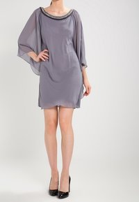 Krátké šedé šaty z lehkého materiálu s lodičkovým výstřihem, zdobené korálkovými detaily. Mají volné rukávy a A-čkový střih.