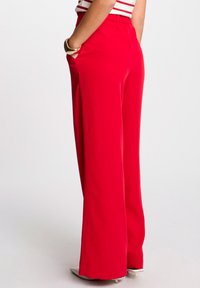Pantalons larges rouges avec taille élastique, dotés de poches latérales et d'une texture lisse. Associés à un top rayé et des talons.
