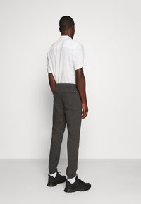 Šedé zúžené kalhoty s elastickým pasem a boční kapsou, spárované s bílým tričkem s krátkým rukávem a černými teniskami.