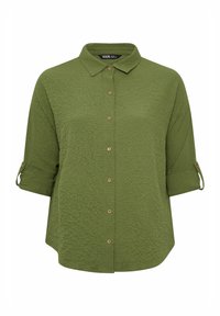 Camicia verde con bottoni, realizzata in un tessuto a trama, maniche arrotolabili e bottoni in legno sul davanti. Orlo leggermente arrotondato nella parte inferiore.
