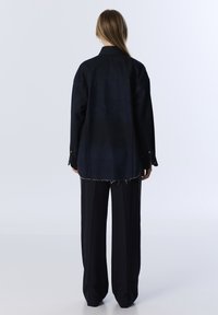 Camicia di jeans scuri con colletto button-down, maniche lunghe e orlo sfrangiato, abbinata a pantaloni neri larghi. Design semplice e funzionale.