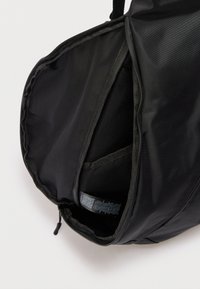Sac à dos noir ouvert montrant un compartiment principal vide avec une pochette rembourrée pour ordinateur portable et une fermeture éclair.