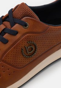Baskets en cuir marron avec un tissu texturé au col, lacets navy, design perforé et un accent logo circulaire sur le côté.