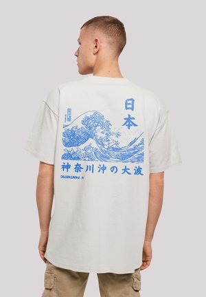 T-shirt en coton blanc avec un grand graphique bleu de vagues et du texte japonais au dos, avec une coupe décontractée et des manches courtes.