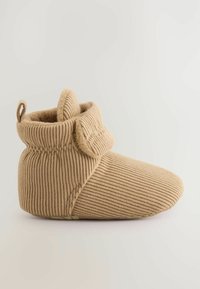 Pantoufle en tissu beige avec texture côtelée, revers plié et petite boucle au dos. Présente un bout lisse et un intérieur doux.