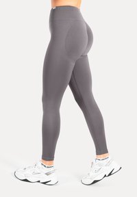 Leggings grigi a vita alta con una texture liscia e una vestibilità sagomata sul corpo, caratterizzate da un dettaglio a cucitura e indossate con scarpe sportive bianche.