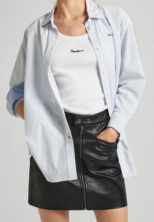 Woman wearing a white tank top with "Pepe Jeans" logo, loose striped button-up shirt, and black leather skirt with front zipper and pockets.