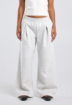 Persoon draagt lichtgrijze wijde broek met elastische tailleband, gecombineerd met zwarte schoenen met vierkante neus en een witte cropped top.