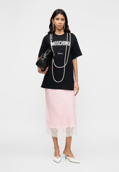 Μαύρο υπερμεγέθες μπλουζάκι με κείμενο "Moschino Milano", σε συνδυασμό με ροζ σατέν φούστα με δαντελένιο τελείωμα. Λευκές μυτερές γόβες και μαύρη τσάντα.