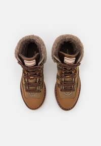 Brown hiking boots with a soft gray lining, textured upper, reinforced toe, and brown laces, featuring a zigzag pattern along the sole.