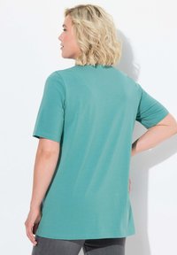 Top turchese a maniche corte con una vestibilità rilassata e un collo rotondo, caratterizzato da una texture liscia e un'orlo posteriore più lungo.