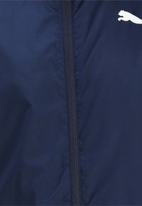 Veste coupe-vent navy avec une fermeture éclair sur toute la longueur à l'avant, ornée d'un logo blanc et d'une texture de tissu lisse et léger.