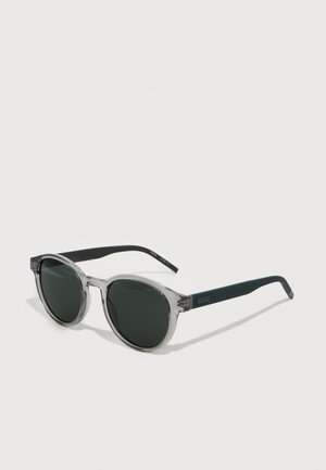 Clear round sunglasses with gray translucent front frames and textured dark green arms, branded "Hugo" on the temples.