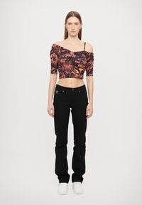 Kort topp i svart og oransje dyremønster med av-shoulder design, kombinert med svarte bukser og hvite sneakers. Tett passform.