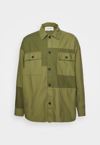 Giacca camicia verde oliva con due tasche sul petto, bottoni neri e vestibilità rilassata. Realizzata in cotone con una superficie liscia e opaca.