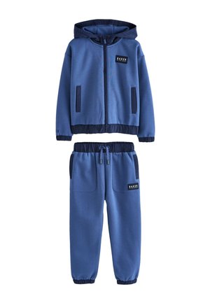 Blåt to-delt træningssæt med hættetrøje med lynlås og elastiske bukser med snøre i taljen, med sort kant og "Baker by Ted Baker" logo patches.