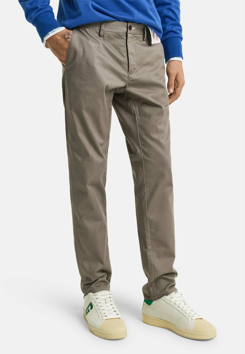 Grå bomullsblandning byxor med slim fit, slät front, sidofickor och en mjuk textur, parat med vita sneakers med gröna detaljer.