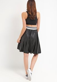 Gonna nera plissettata con fascia a righe in vita, realizzata in materiale leggero; presenta un design fluido e una texture morbida. Abbinata a sneakers bianche.