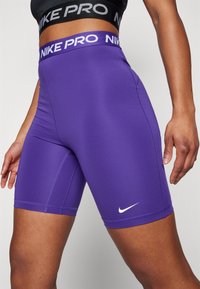 Shorts violets Nike Pro avec une finition texturée, présentant une large taille étiquetée "NIKE PRO" en blanc et un petit logo Nike blanc.