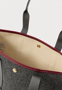 Γκρίζα tote bag με μπορντώ λεπτομέρειες, μπεζ εσωτερικό, γκρίζες υφασμάτινες χερούλες και χρυσό κουμπί snap κλεισίματος, ελαφρώς ανοιχτή.