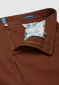 Bruine chino broek van stevige stof, met een ritssluiting, knoopsluiting en een gestreepte voering met blauwe accenten.