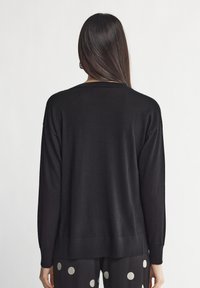 Pull en tricot noir à coupe décontractée, épaules tombantes, poignets et ourlet côtelés. Pas de motifs visibles ni de détails matériels distinctifs.