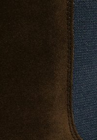 Cucitura in suede marrone e tessuto blu scuro testurizzato, caratterizzata da un bordo liscio e materiali a contrasto. Leggero luccichio nell'area blu.