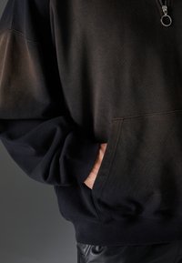 Felpa con zip nera e grigia scura, con tasca a marsupio, vestibilità comoda, polsini a costina e una texture liscia.