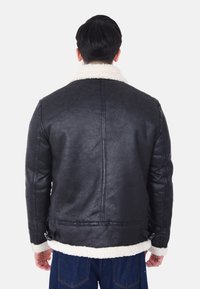 Giacca di pelle nera con colletto e polsini in shearling bianco, caratterizzata da una superficie liscia e regolatori laterali vicino all'orlo.