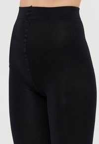 Juodos leggingos su aukštu juosmeniu, lygiu paviršiumi ir prigludusia išvaizda. Išsiskiria subtiliu blizgesiu ir nematomomis siūlėmis.