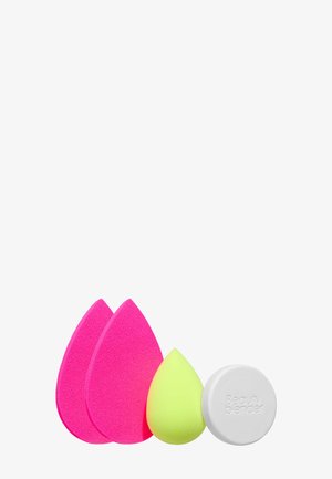 Dwie różowe gąbeczki w kształcie łzy, jedna mniejsza żółta gąbeczka w kształcie łzy oraz okrągły biały środek do czyszczenia Beauty Blender.