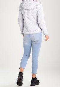 Giacca trapuntata grigia chiara con cappuccio, con dettagli rosa, abbinata a jeans azzurri aderenti e sneakers nere.