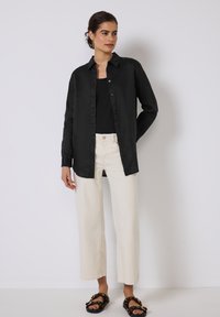 Camisa de lino negra con botones en el frente, combinada con pantalones anchos color crema. Las sandalias tienen una correa gruesa y detalles decorativos.