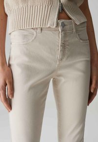 Jean skinny beige en denim lisse avec poches avant et fermeture à bouton, présentant des détails de couture subtils le long des coutures.