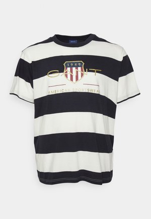 T-shirt à manches courtes à larges rayures noires et blanches avec un logo en forme de bouclier et le texte « GANT 1949 American Sportswear » sur la poitrine.