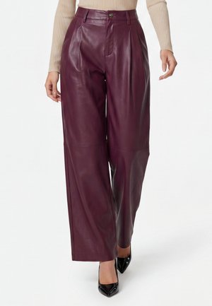 Donna che indossa pantaloni in pelle bordeaux a vita alta e gamba larga, top beige a coste e tacchi neri con punta appuntita mentre cammina in avanti.