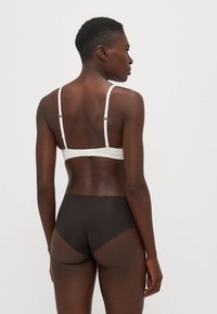 Witte bh met verstelbare bandjes en een sluiting op de rug, gecombineerd met donkerbruine high-waisted slipjes met een gladde, matte textuur.