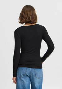 Črn dolg rokav vrh z teksturirano površino, okroglo ovratnikom in slim fit krojem, v kombinaciji z ohlapnimi jeans hlačami.