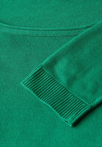 Tissu en tricot vert pour pull, gros plan montrant une texture lisse et des poignets côtelés. Points forts : un design simple et classique.