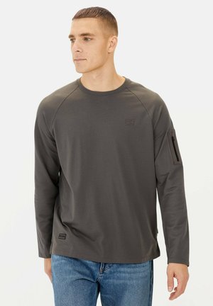 Gray long-sleeve shirt with a round neck, raglan sleeves, chest logo patch, and zip pocket on left sleeve. Smooth texture, casual design.