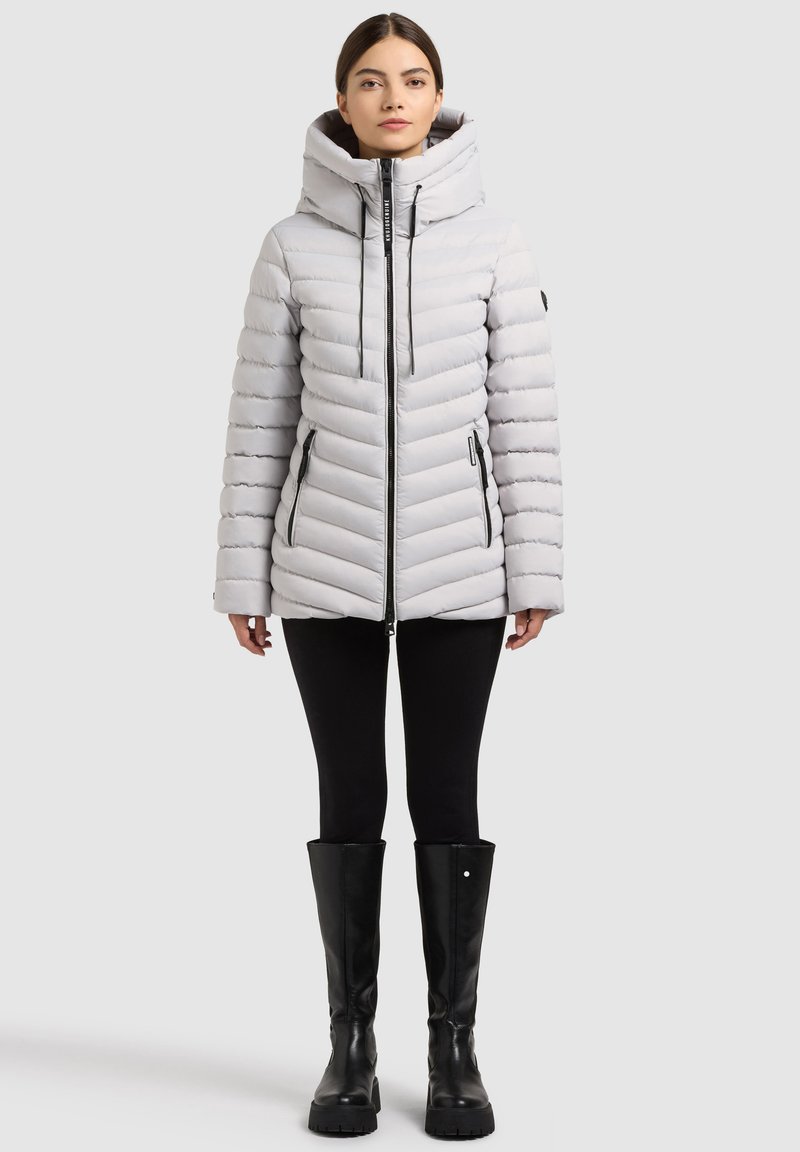 Světle šedá péřová bunda s vysokým límcem a kapucí, zdobená diagonálními prošitými liniemi, dvěma předními kapsami na zip a černými prvky.