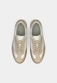 Beige en witte sneaker met suède en leren panelen, uitgerust met een ronde neus, vetersluiting en een gestructureerde rubberen zool.