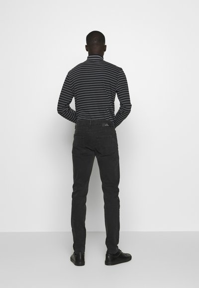 Chemise à rayures noires à manches longues associée à un jean foncé. La chemise présente un col haut et un design ajusté, avec un pantalon slim et des chaussures noires.