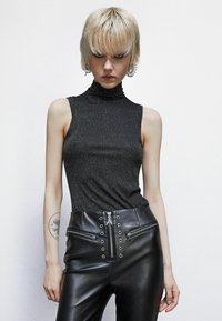 Top nero senza maniche con un collo alto e rigato, realizzato in tessuto luccicante. Abbinato a pantaloni in pelle neri a vita alta e slim con tasche con zip.